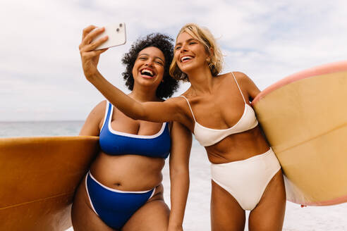 Zwei Freundinnen im Bikini halten ihren Strandurlaub mit einem Selfie fest und verkörpern so den Geist der Freundschaft und die gemeinsame Freude am Wellenreiten - JLPSF30658