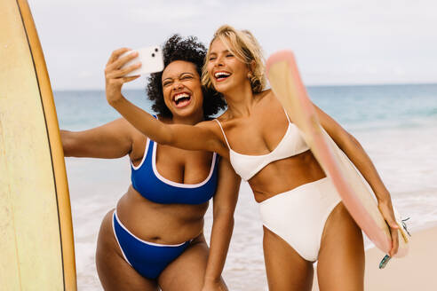 Zwei Frauen im Bikini fangen die Essenz des Sommers ein, als sie während eines Surfurlaubs ein lebhaftes Selfie am Strand machen - JLPSF30660