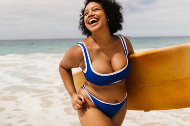 Eine kurvige junge Frau genießt die Aktivitäten am Strand und feiert den Sommer auf einem Solo-Urlaub. Eine Surferin trägt ein Brett und einen Bikini und fängt die Essenz eines lustigen und authentischen Sommerurlaubs ein. - JLPSF30676