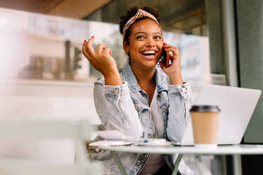 Cheerful businesswoman indoors, using a smartphone for communication. Engaged in a lively discussion, she listens and answers calls on her portable device with enjoyment and happiness. - JLPSF30696