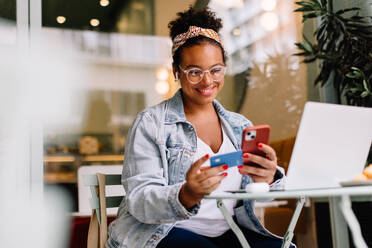 Happy entrepreneur uses a cellphone for online shopping and payment in a cozy café. Technology and business seamlessly combine in this real lifestyle moment. - JLPSF30708