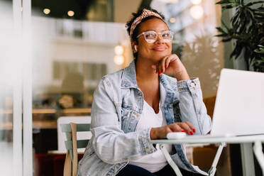 Young woman works remotely in a cozy coffee shop, using a laptop. She is a freelance content writer, focused and pensive as she works on her website writing project. - JLPSF30710