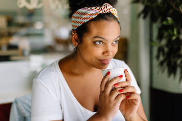 Junge Frau sitzt in einem Café und genießt ein heißes Getränk. Sie hält einen schwarzen Becher und genießt jeden Schluck Kaffee bei diesem entspannenden Einzeldate. - JLPSF30719