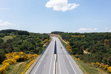 Aerial view of asphalt road with divider and lanes while cars driving on highway and heading through autumn forest with green trees against blue sky on sunny day - ADSF45772