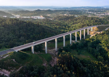 From above highway road bridge for vehicular transport as part of infrastructure development built over valley with green forest trees and hills connecting towns on sunny day - ADSF45775