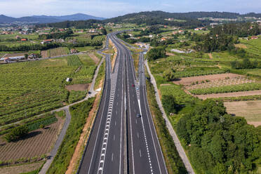 Aerial view of speedway passing through green agriculture fields on sunny day and connecting towns while sideways on highway built for smooth entry and exit points of vehicles - ADSF45781