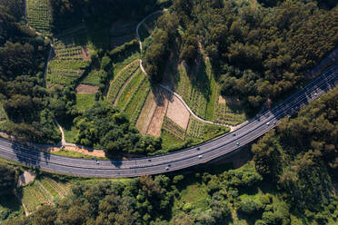 From above aerial view of cars driving on asphalt road with lanes with on valley with agriculture fields while going through green fields in countryside - ADSF45784