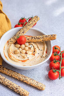 High angle of healthy plant-based plate with hummus and tomatoes served with bread sticks in bowl near napkin against blurred background - ADSF45789