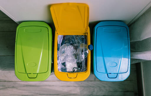 Top view of recycling containers and plastic bottles inside opened yellow recycling trash placed in kitchen - ADSF45809