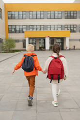 Back view of unrecognizable children with backpack walking towards a school building in daylight - ADSF45825