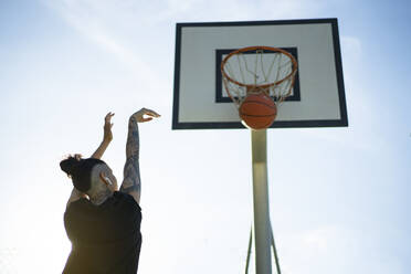 From below back view of anonymous female basketball player throwing ball in hoop on sports ground on sunny day - ADSF45826