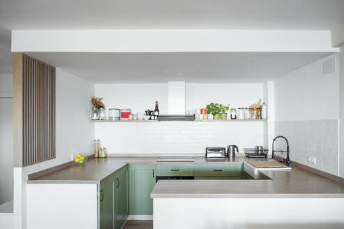 Interior design of contemporary minimal kitchen with marble top and cupboards with appliances and basin, white walls and shelves with bottles - ADSF45836