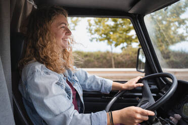 Young female traveler at steering wheel smiling and driving car of window while looking away at road through windshield - ADSF45856