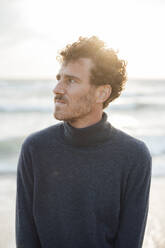 Thoughtful man wearing turtleneck sweater standing at beach - JOSEF20332