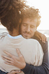 Mann mit geschlossenen Augen umarmt Freundin am Strand - JOSEF20351