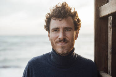 Smiling man wearing turtleneck sweater at beach - JOSEF20373