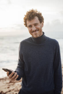 Lächelnder Mann mit Smartphone am Strand - JOSEF20378