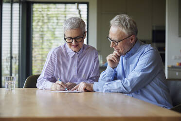 Senior couple sitting at table at home examining document - RBF09115