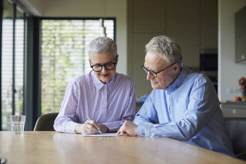 Senior couple sitting at table at home examining document - RBF09116