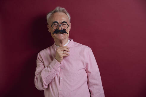 Älterer Mann posiert mit falschem Schnurrbart vor lila Hintergrund - RBF09124