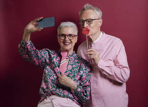 Happy senior couple with fake lips and tie taking selfie - RBF09128