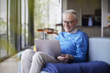 Senior man sitting on couch at home using tablet PC - RBF09131