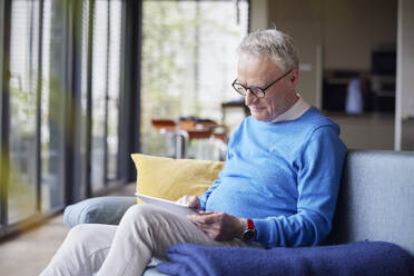 Älterer Mann sitzt zu Hause auf der Couch und benutzt einen Tablet-PC - RBF09133