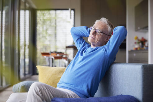Älterer Mann sitzt zu Hause auf der Couch mit den Händen hinter dem Kopf - RBF09134