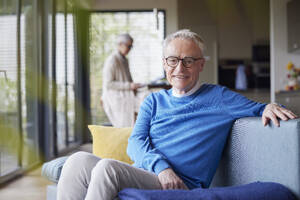 Porträt eines lächelnden älteren Mannes, der zu Hause auf der Couch sitzt - RBF09135