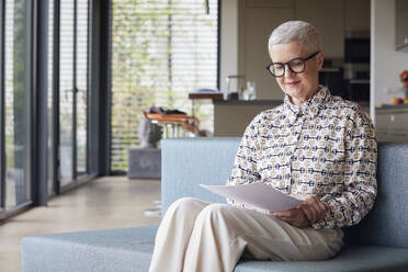 Senior woman sitting on couch at home reading document - RBF09150