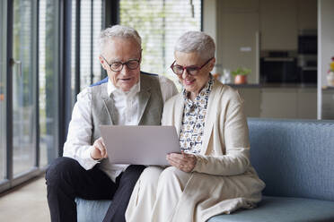 Senior couple sitting on couch at home using tablet PC - RBF09153