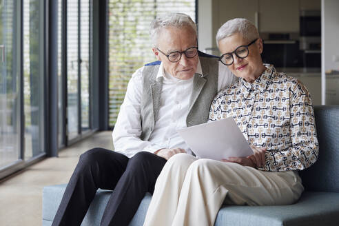 Senior couple sitting on couch at home reading document - RBF09155