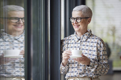 Lächelnde ältere Frau mit einer Tasse Kaffee und Blick aus dem Fenster - RBF09167