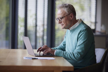 Senior man using laptop at table at home - RBF09193