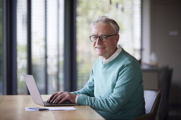Portrait of smiling senior man using laptop at table at home - RBF09195