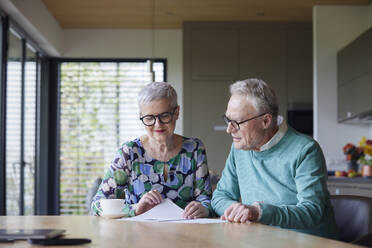 Senior couple sitting at table at home examining document - RBF09211
