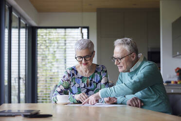 Älteres Ehepaar sitzt zu Hause am Tisch und prüft ein Dokument - RBF09212