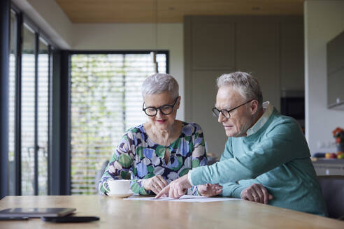 Senior couple sitting at table at home examining document - RBF09212