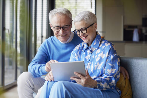 Glückliches älteres Paar sitzt zu Hause auf der Couch und benutzt einen Tablet-PC - RBF09230