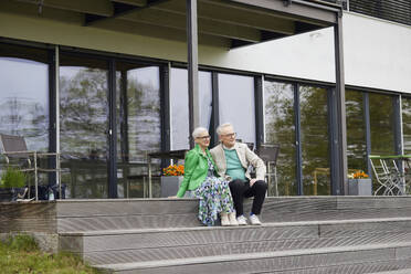 Senior couple sitting on steps in front of their home - RBF09246