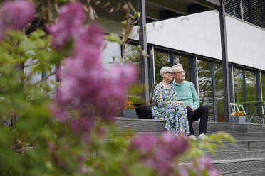 Senior couple sitting on steps in front of their home - RBF09257