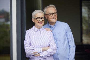 Happy senior couple standing at balcony door - RBF09264
