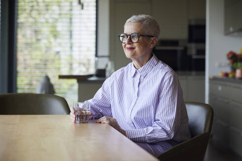 Selbstbewusste ältere Frau, die zu Hause am Tisch sitzt - RBF09265