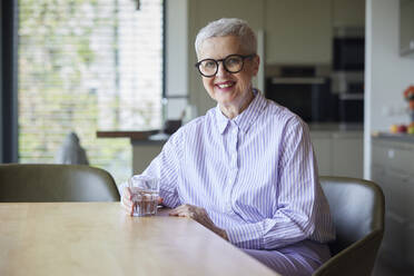 Portrait of smiling senior woman sitting at table at home - RBF09266