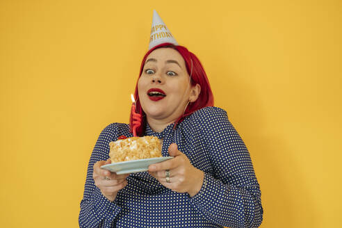 Surprised woman holding birthday cake against yellow background - OSF01916