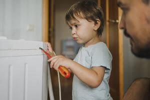 Vater beobachtet Sohn bei der Reparatur einer Waschmaschine zu Hause - ANAF01842