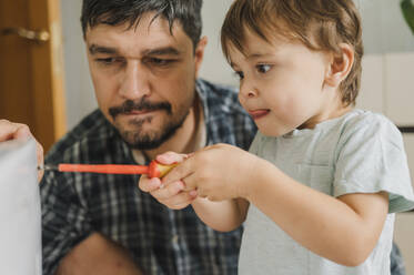 Father watching son repairing washing machine at home - ANAF01846