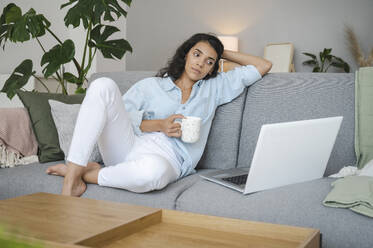 Young woman relaxing and watching movie on laptop at home - ALKF00489