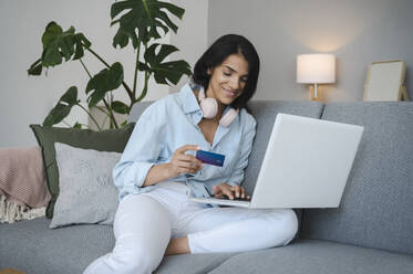 Lächelnde Frau beim Online-Shopping mit Kreditkarte zu Hause - ALKF00496