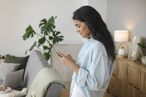 Junge Frau benutzt ein Smartphone im Wohnzimmer zu Hause - ALKF00499